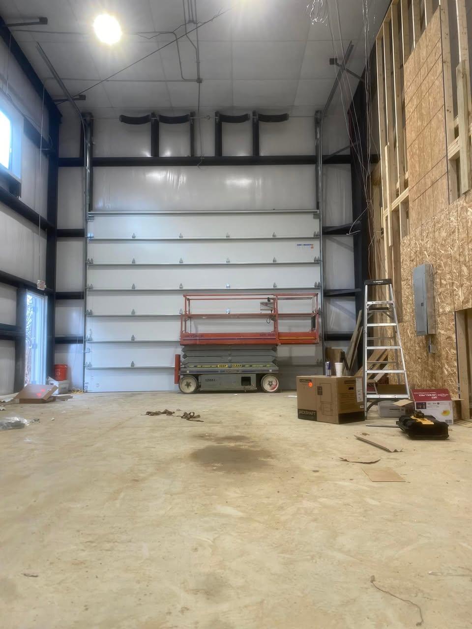 High-lift commercial overhead door installation with scissor lift inside a steel building
